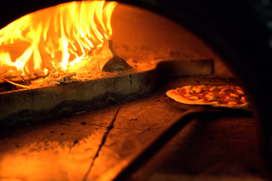 A pizza being placed in a wood-fired pizza oven